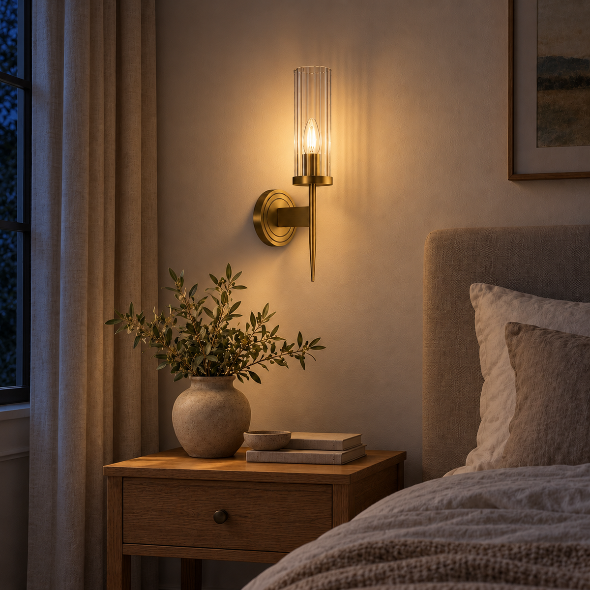 Slender Fluted Glass Torch Wall Light above a wood bedside table beside an upholstered bed at night, illuminated