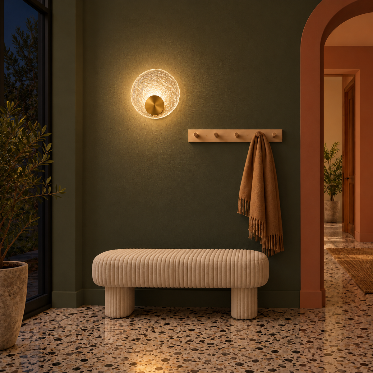 Textured glass disc wall light glowing above a pale upholstered bench at night