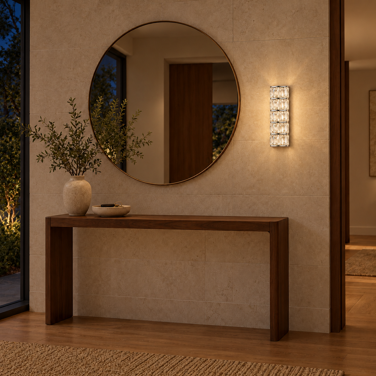 Five Tier Crystal Column Wall Light illuminated beside a round mirror above a wooden entry console at night