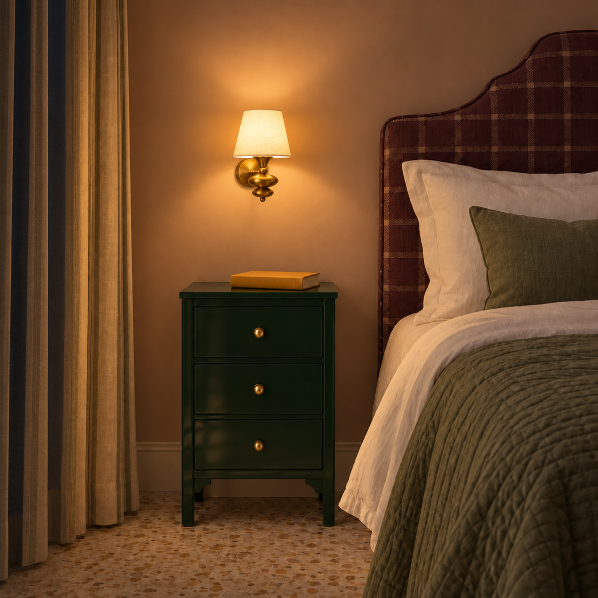 White shade sculpted-finial wall light illuminated beside an upholstered bed at night