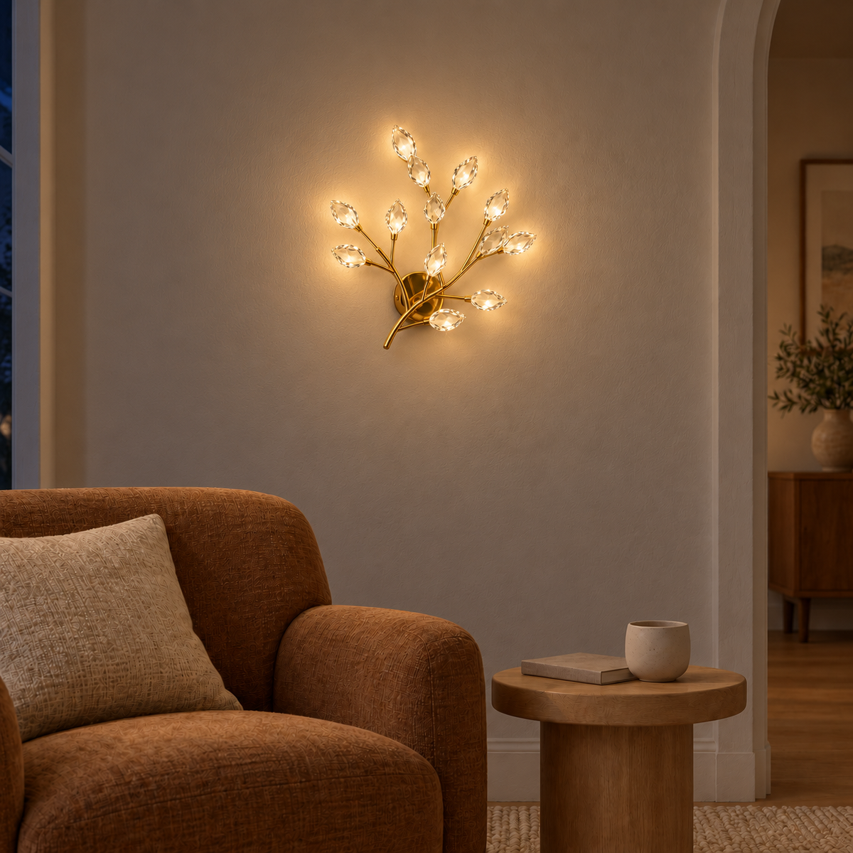Crystal leaf branch wall light illuminated above a side table beside an upholstered armchair at night
